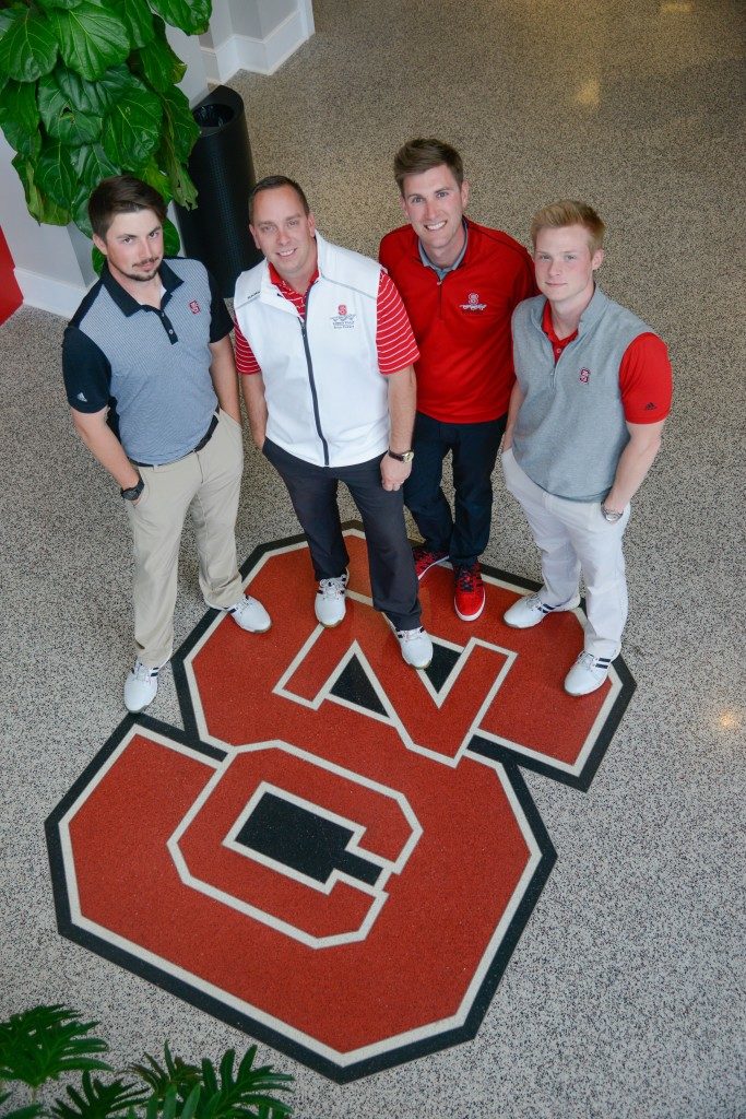 Player development staff standing on an NC State logo floor.