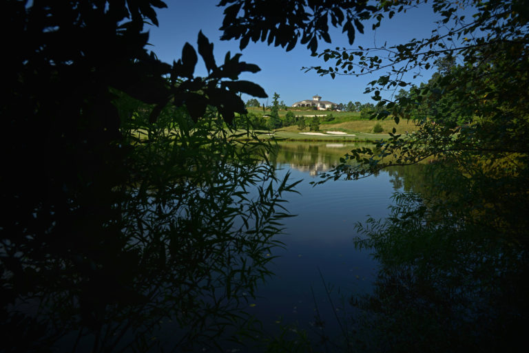 A shaded pond, with a golf fairway and the clubhouse in the distance.