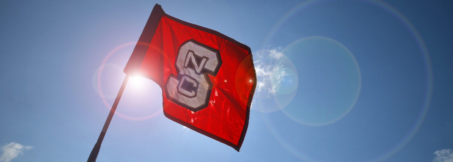 A red flag with an NC State block S is illuminated from behind by the sun.