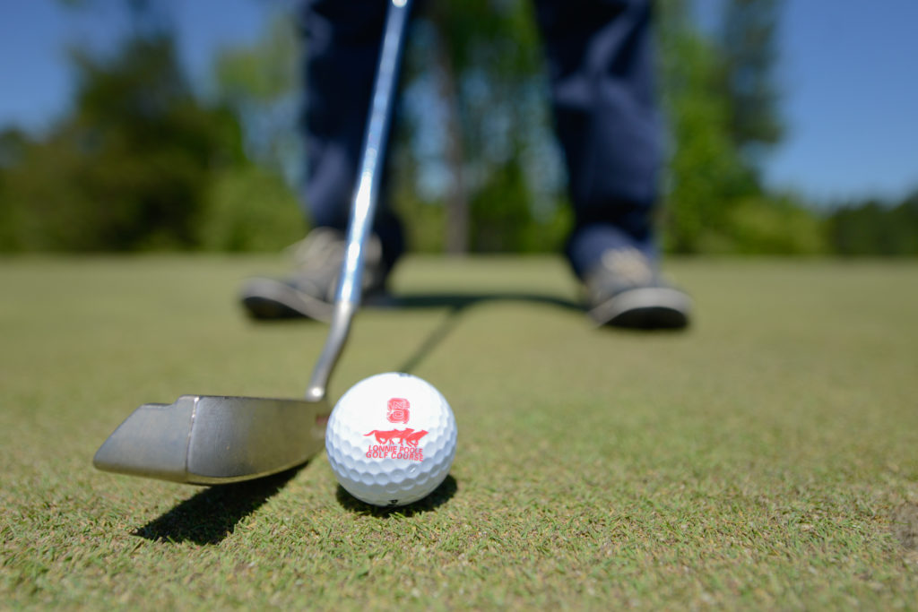 A golfer prepares to hit a golf ball with the Lonnie Poole Golf Course logo on it.